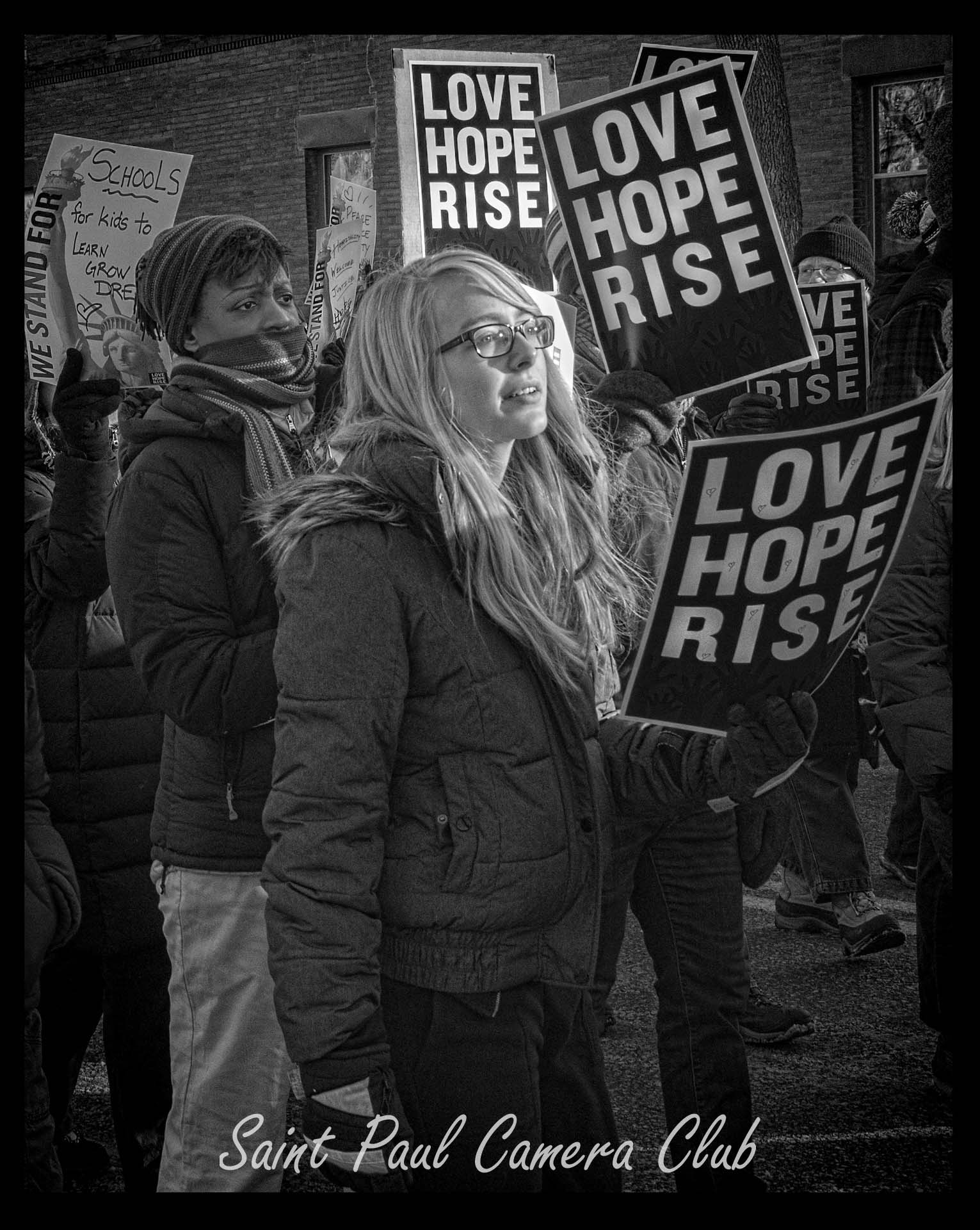 People holding "Love Hope Rise" signs at a demonstration.